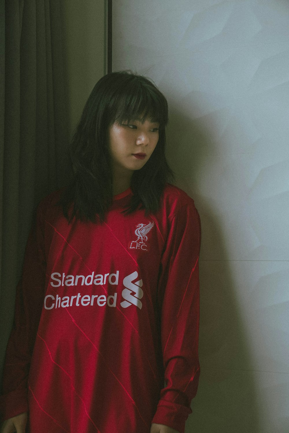 a woman in a red liverpool shirt leaning against a wall