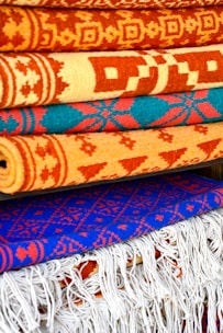 Close-up of vibrant, handwoven rugs stacked neatly in a workshop.