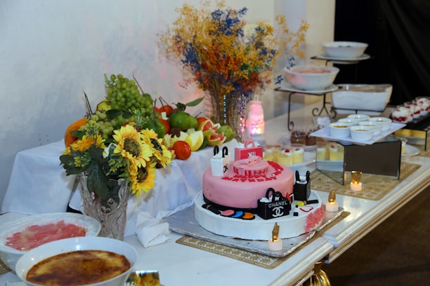 a table topped with a pink cake next to a bowl of fruit
