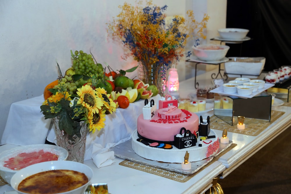 a table topped with a pink cake next to a bowl of fruit