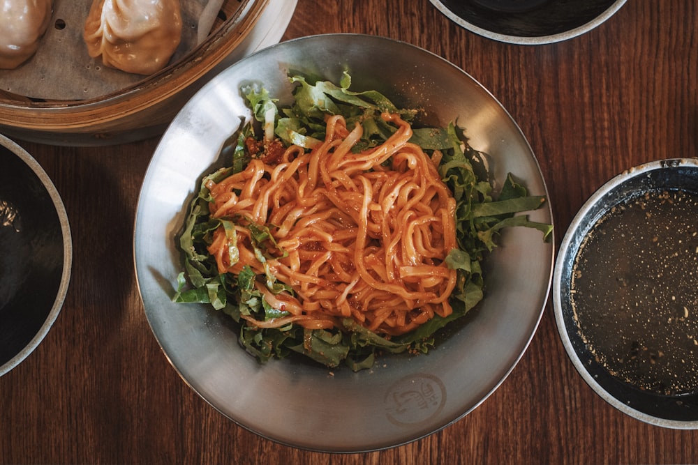 a bowl of noodles and greens on a table