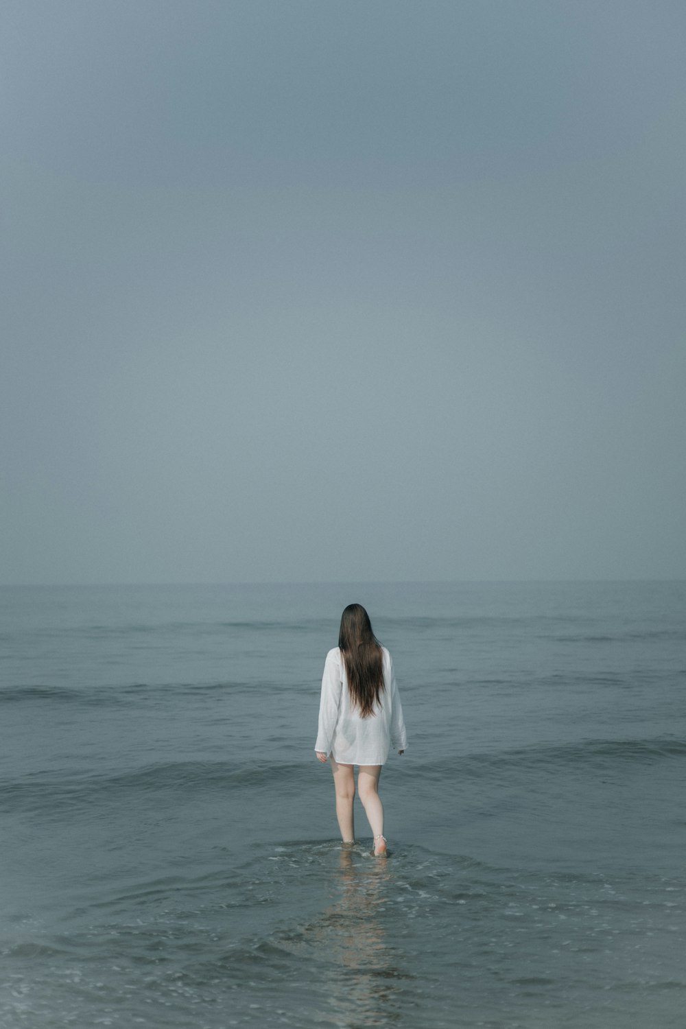 a woman standing in the ocean looking at the horizon
