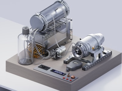 A complex mechanical apparatus consisting of metallic components including a cylindrical tank, a series of tubes, and a turbine. The setup is mounted on a flat platform with digital and analog controls embedded on the surface. The device appears to be part of an engine or a mechanical test bench, with a large transparent bottle and an array of wires visible.