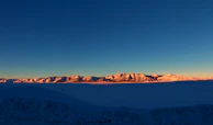Wide shot of a vast ice mountain range glowing softly at dawn.