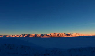 Wide shot of a vast ice mountain range glowing softly at dawn.