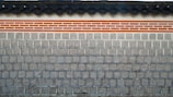 A traditional stone wall featuring a layer of clay bricks highlighted with orange and white colors. The top of the wall displays a series of dark gray, rounded roof tiles, which add a distinct architectural element.