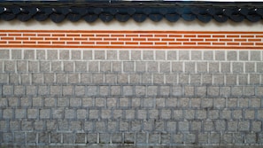 A traditional stone wall featuring a layer of clay bricks highlighted with orange and white colors. The top of the wall displays a series of dark gray, rounded roof tiles, which add a distinct architectural element.