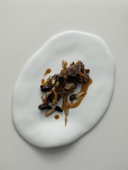 A minimalist presentation of gourmet food on a unique white plate. The dish appears to include a variety of mushrooms and a drizzle of sauce, artfully arranged.