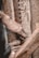 A person is engaged in wood carving, using a chisel to intricately engrave patterns into a piece of wood. The hands are weathered, suggesting experience or age, and the focus is on the detailed craftsmanship. There is a close-up view of tools and the carved wooden surface.