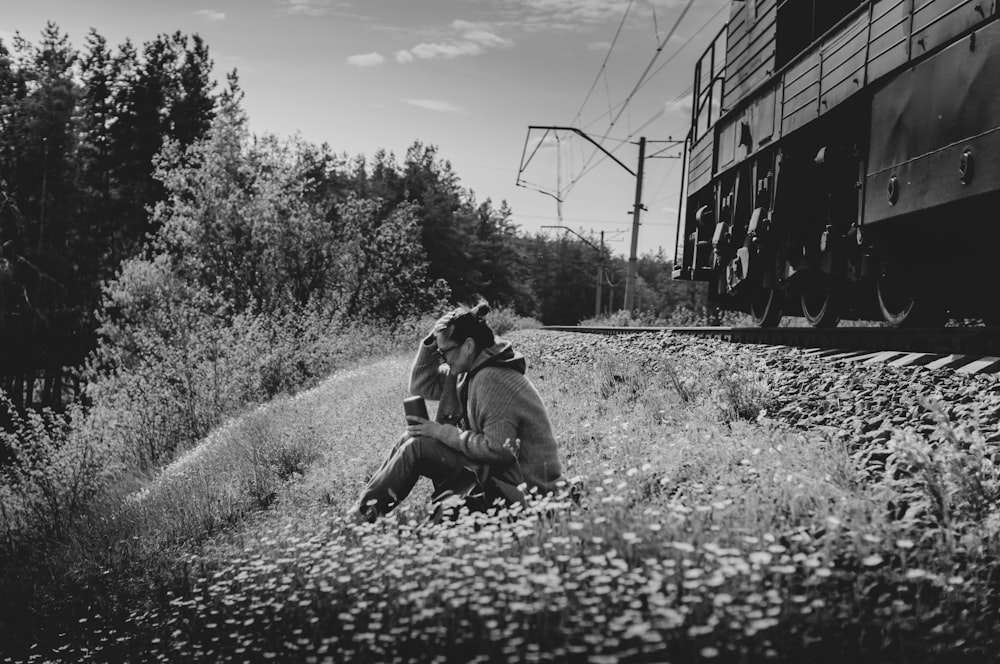 a man and a woman sitting on the ground next to a train
