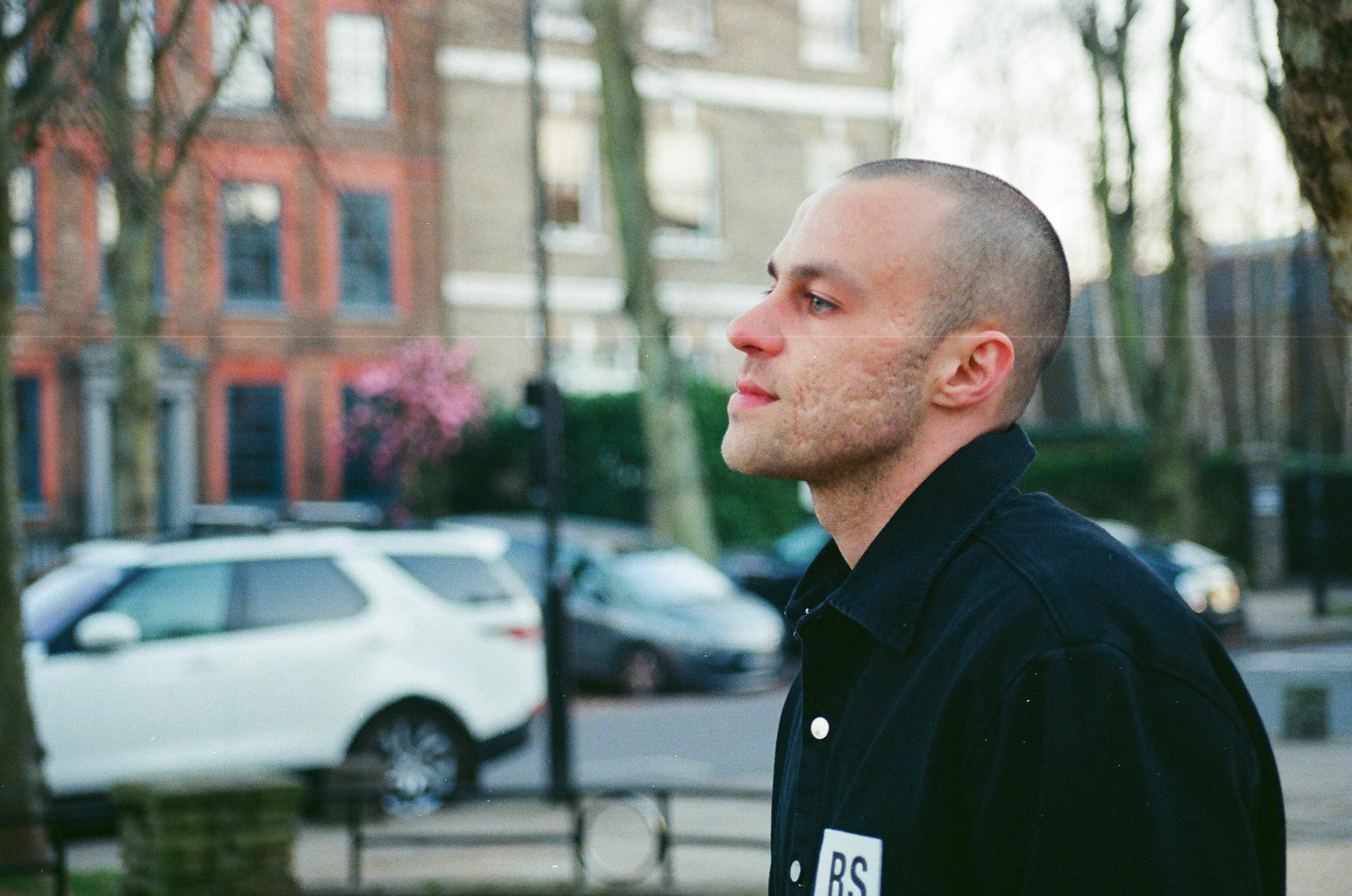 a man in a black shirt standing in front of a tree