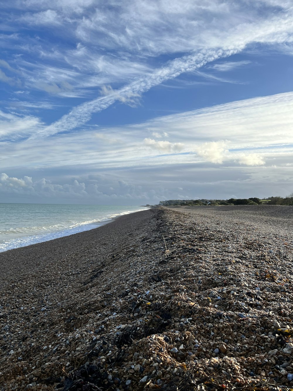 a sandy beach next to the ocean under a cloudy blue sky