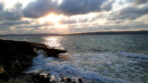 A beautifully framed coastal photograph capturing the golden light of sunset over Cape Ann's rocky shore.