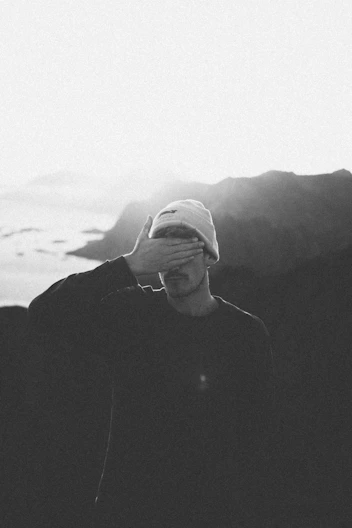 a black and white photo of a man covering his eyes