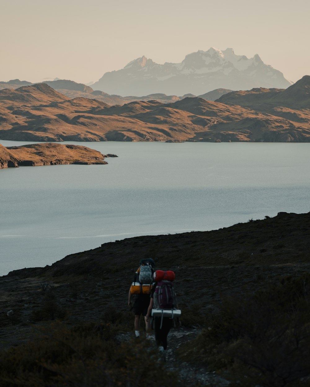 two people with backpacks walking up a hill towards a body of water