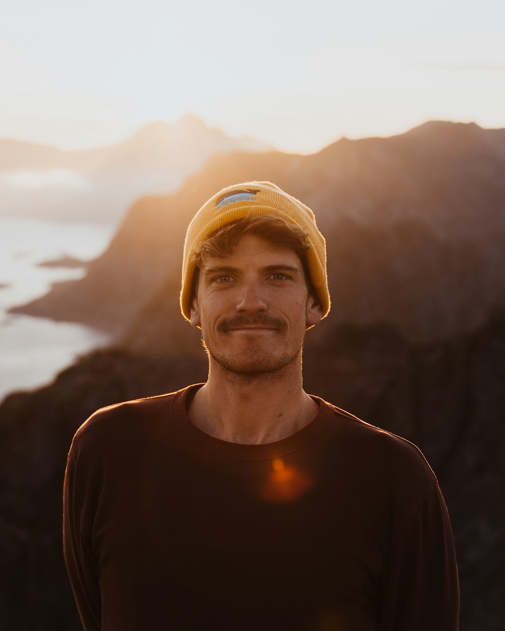 a man wearing a yellow hat standing in front of a mountain