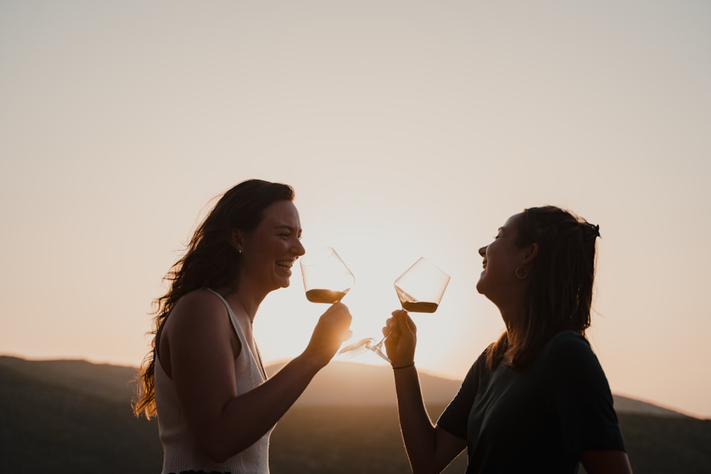 um casal de mulheres em pé um ao lado do outro segurando taças de vinho