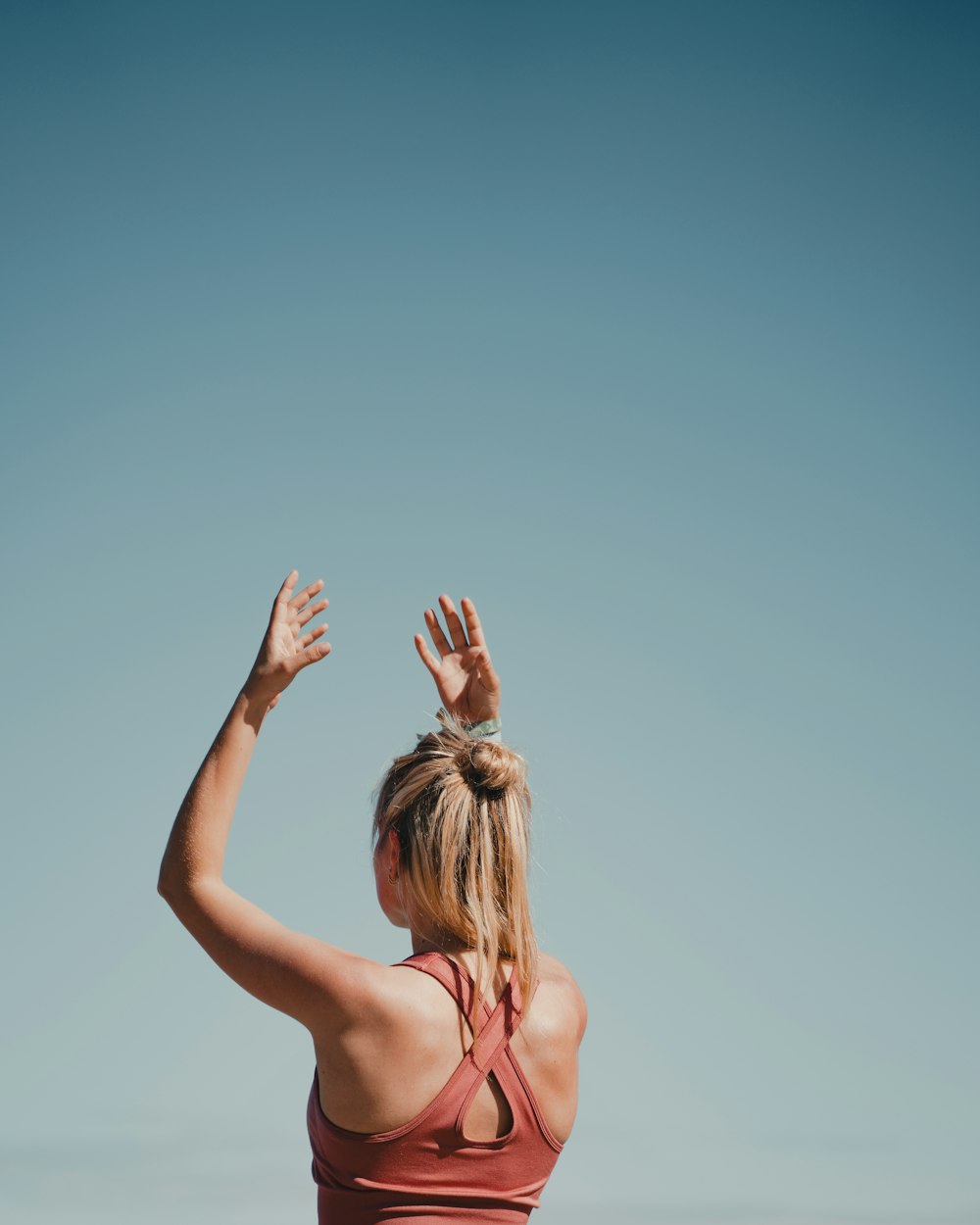 a woman in a red tank top reaching up into the sky