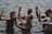 A group of people standing in water are engaged in a dance or meditative activity, with their eyes closed and hands raised in expressive gestures.
