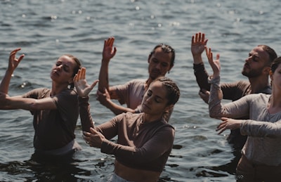 A group of people standing in water are engaged in a dance or meditative activity, with their eyes closed and hands raised in expressive gestures.