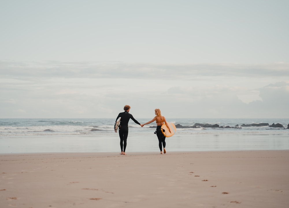 Un hombre y una mujer tomados de la mano mientras caminan por la playa