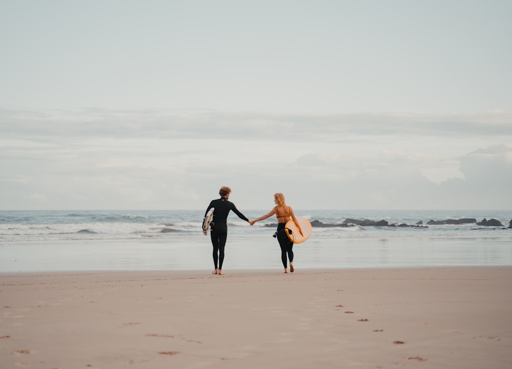 a man and a woman holding hands while walking on the beach