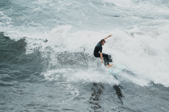 A surfer skillfully navigates through a breaking wave, leaning confidently on their board. The ocean is turbulent, with foamy white crests and dark, swirling waters.