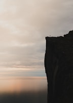 Silhouette of a lone figure standing on a cliff edge beneath a brooding sky.