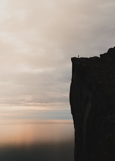 Silhouette of a lone figure standing on a cliff edge beneath a brooding sky.