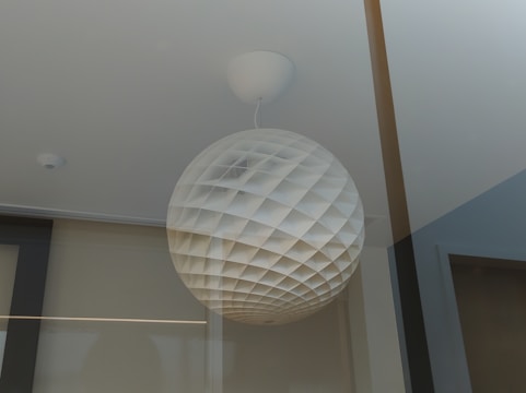A spherical light fixture with a geometric lattice pattern is hanging from the ceiling. The design creates a dynamic interplay of light and shadow, suggesting a modern and minimalist aesthetic.