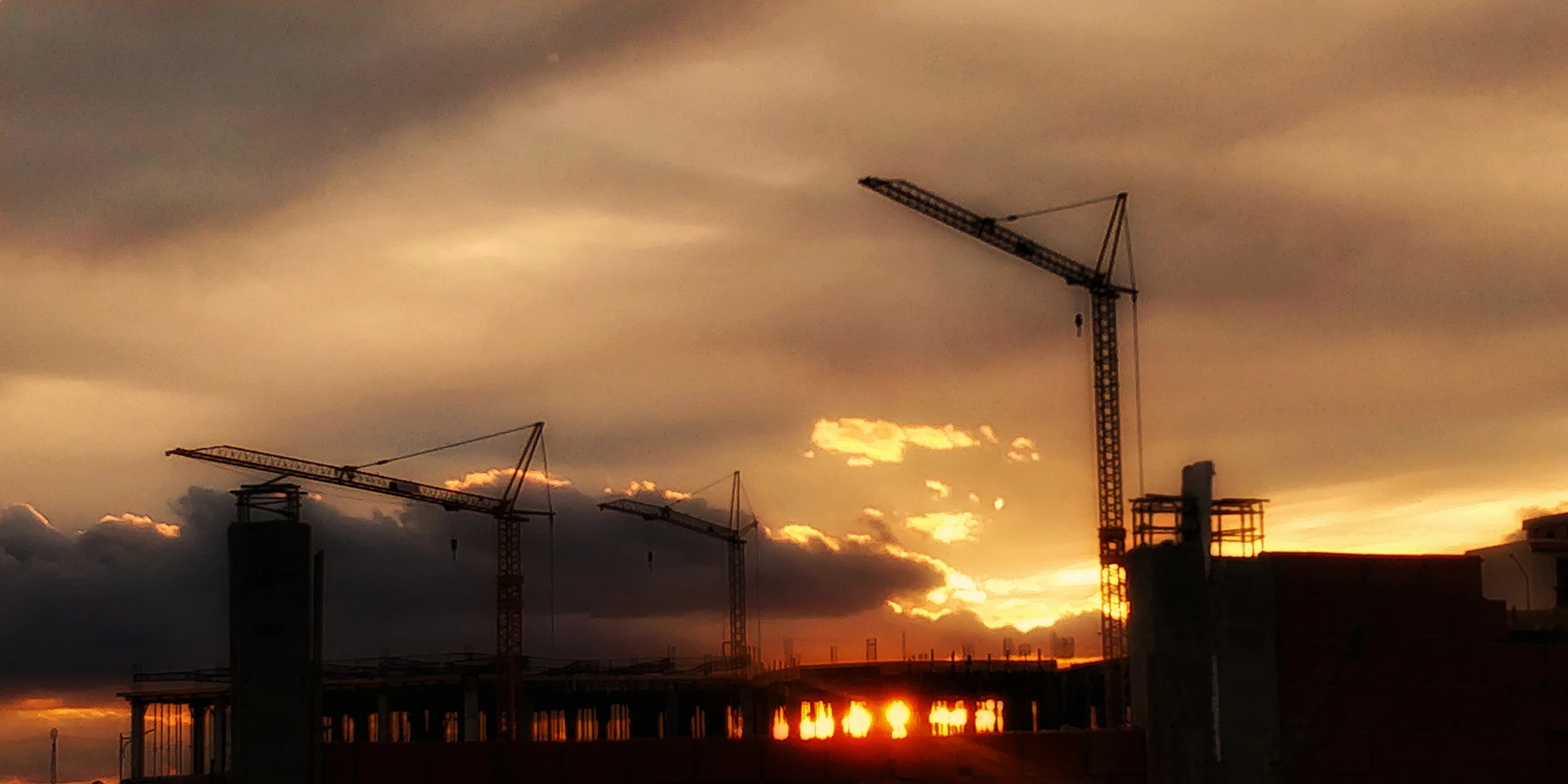 A majestic construction site at sunset showcasing heavy machinery and workers collaborating on a high-rise building frame.