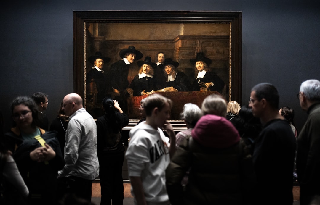 a group of people standing in front of a painting, People admiring art in museum at Rijksmuseum in Amsterdam