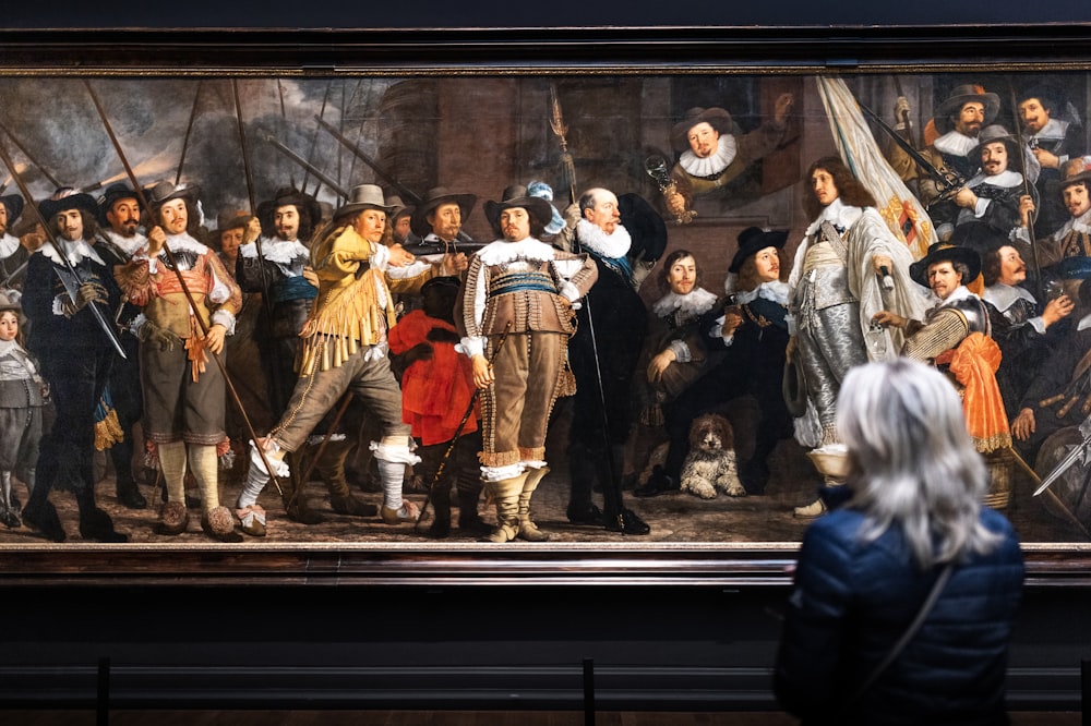 eine Frau steht vor einem Gemälde einer Gruppe von Menschen