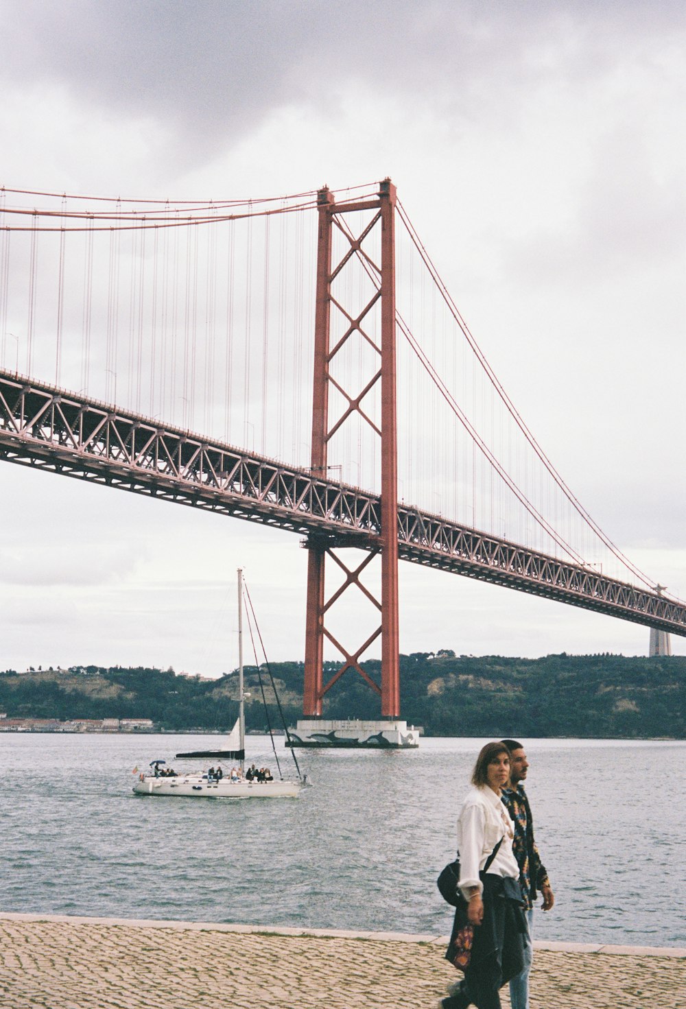 un uomo e una donna che camminano su una spiaggia vicino a un ponte
