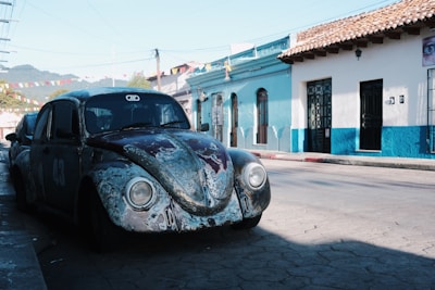 A colorful vintage Volkswagen Beetle parked on a sunny street with retro-style clothing displayed nearby.