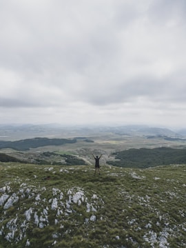 A man standing at sunrise on a hilltop, arms raised in triumph.