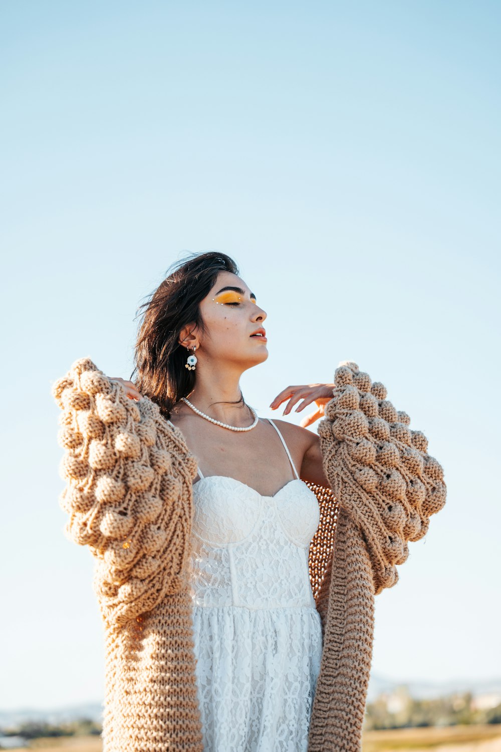 a woman wearing a white dress and a brown cardigan