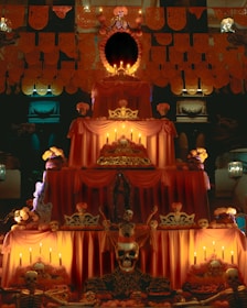An elaborate altar decorated with marigold flowers and candles, typically used during the Day of the Dead celebrations. The altar is layered and adorned with intricate paper cut-out designs, a variety of skulls, and skeleton figures. The setting is illuminated by the warm glow of numerous candles.