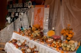 An altar is adorned with colorful decorations, including marigold flowers, papel picado, and various offerings like fruits, bread, and candles. Small skulls are placed around, and a poster remembers beloved pets.