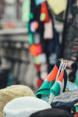 A close-up view of small flags in red, green, black, and white. These are positioned among various items such as plush garments, with blurred colorful fabrics in the background.