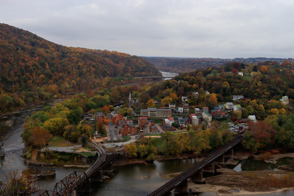 Harpers Ferry from above in autumn, with the river, its railroad bridges and wooded ridges behind