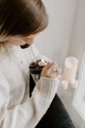 A person is using a glass bong, holding a lighter to ignite the contents. The setting appears cozy, with a soft sweater and candles nearby creating a warm ambiance.