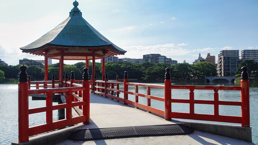 a red wooden gazebo sitting next to a body of water