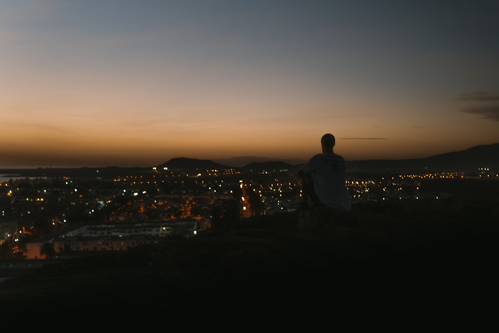 a man sitting on top of a hill overlooking a city