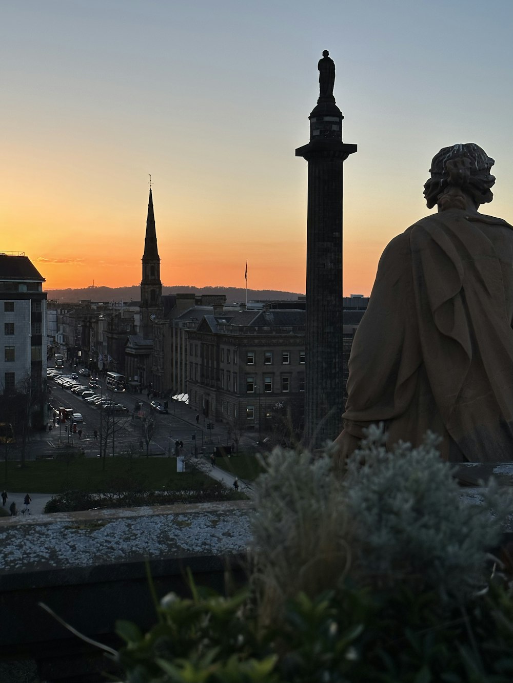 a statue of a person overlooking a city at sunset