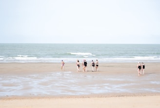 A group of women laughing and walking along the shoreline, each wearing different manaia swimwear styles.