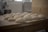 Several pieces of dough are neatly arranged on a wooden table in a kitchen setting, preparing them for baking. In the background, blurred elements of a mixing appliance can be seen, suggesting a professional or home-like baking environment.