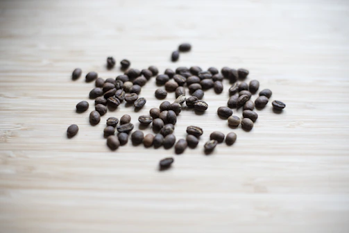 Artistic shot of coffee beans scattered on natural wood with soft shadows.