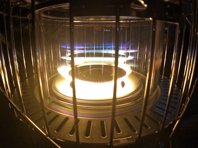 A close-up of a glowing heater element surrounded by a protective metal cage. The element emits a bright white and yellow light with hints of blue at the edges.