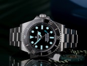 A luxury wristwatch with a luminous dial and markers, featuring a stainless steel bracelet and a rotating bezel. The watch face is adorned with the brand logo, offering a sleek and polished appearance against a dark background.